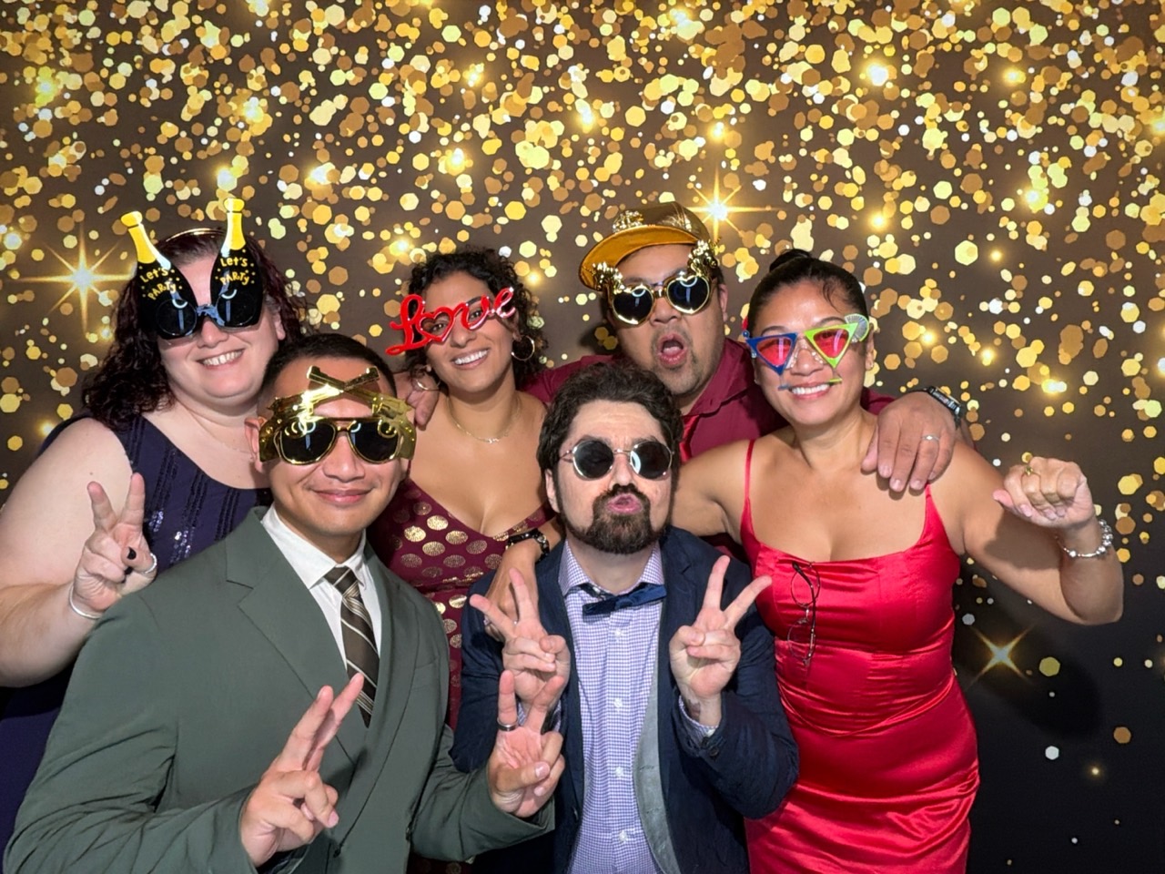 Invités d’un mariage posant avec des accessoires devant le fond doré du photobooth numérique